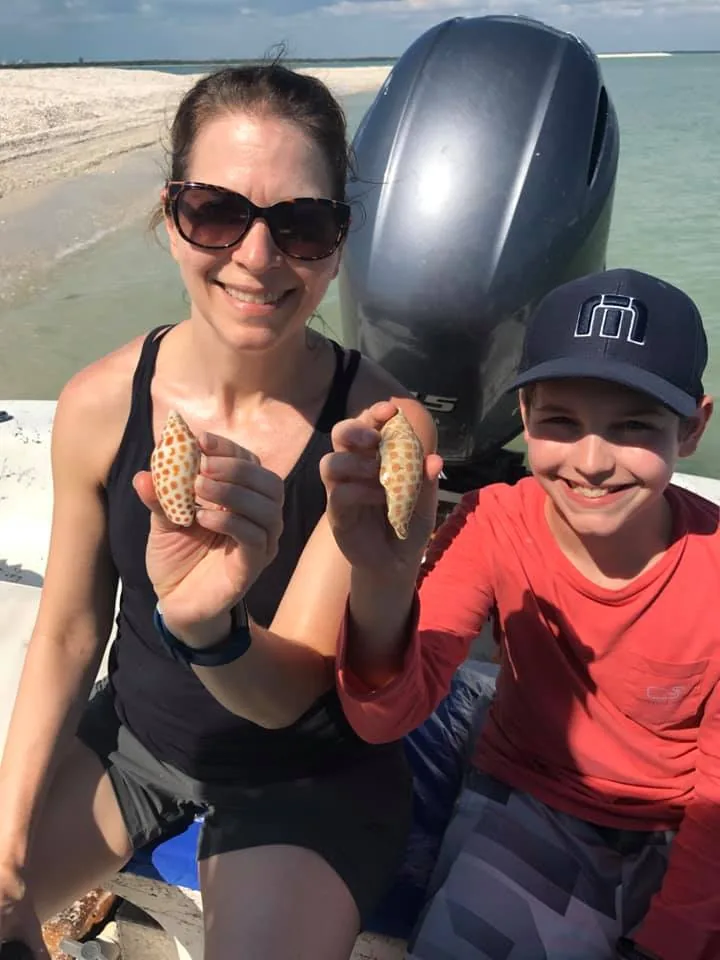 A woman in sunglasses and a boy in a red shirt each hold up a shell on the boat